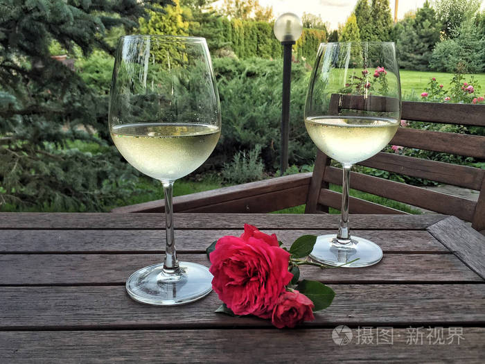 夏日花园木桌上的酒杯和玫瑰花