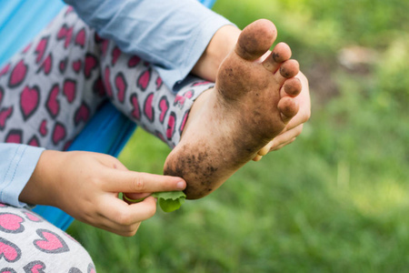 孩子赤脚走在草地上, 她肮脏的脚照片