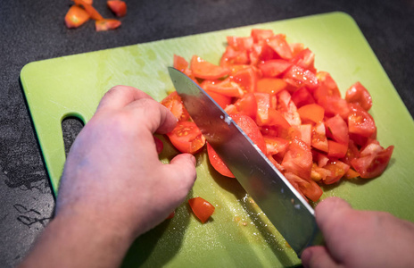 在绿色砧板上用刀子切西红柿的厨师