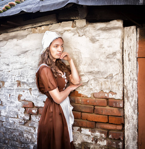 忧郁的年轻女子穿着一件土气的连衣裙站在老房子的旧砖墙上感到孤独。灰姑娘风格
