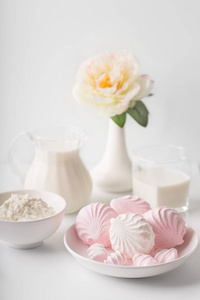 在白色的背景下, 一杯牛奶, 一盘棉花糖, 奶酪, 牛奶壶和牡丹在花瓶里。工作室灯高键。选择性焦点