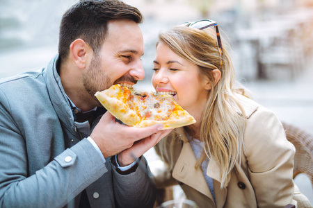 快乐的爱情情侣一起吃披萨片在街头咖啡馆
