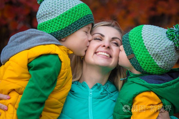 两个小男孩轻轻地拥抱和亲吻你心爱的母亲在秋天的树林里漫步