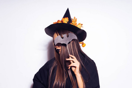 一个年轻的哥特式女孩庆祝万圣节，在黑色的帽子，装饰着黄色的树叶，覆盖她的脸与头发和蝙蝠的绘图
