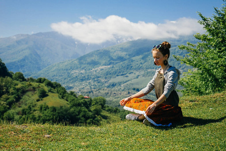 美丽的时尚女孩坐在绿色的草地上, 背靠高山的背景, 享受自然冥想和放松