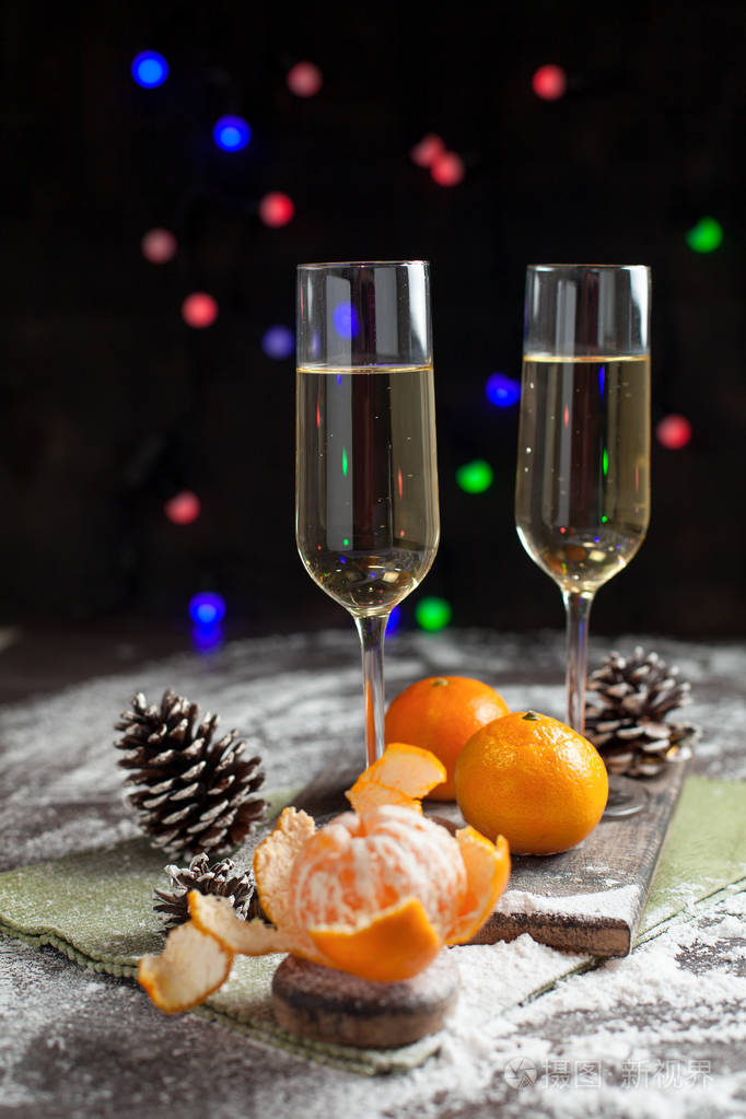 在一个白色的盘子上的新年餐桌上的橘子, 颠簸和眼镜, 香槟, 绿色的餐巾和新年的灯在黑暗的背景