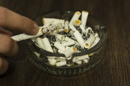 熄灭的烟头烟头在一个玻璃烟灰缸.一只手捧着一支香烟, 不熄灭照片