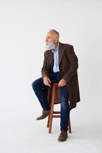 坦率成熟的胡子男子在大衣坐在椅子上工作室
