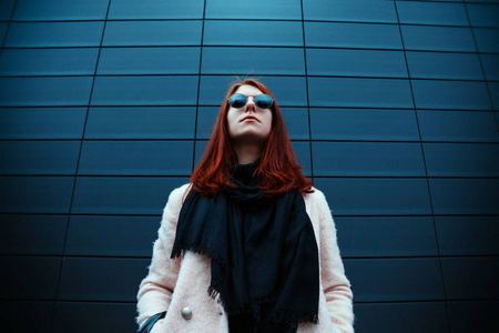 时髦的 redhaired 女孩在时尚的太阳镜是摆在前面的黑色墙壁在街上