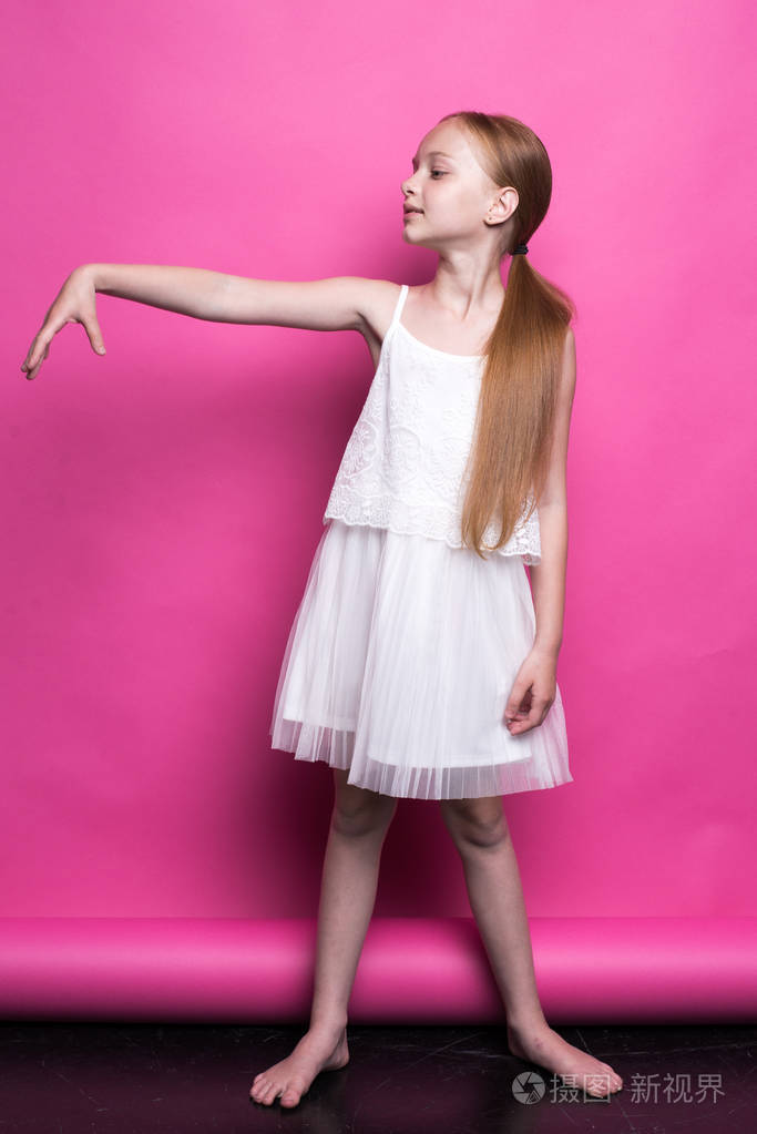 美丽的红头发的小女孩穿白色连衣裙,像粉红色背景模型构成