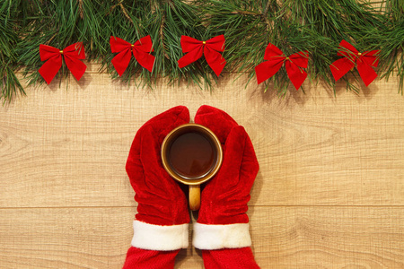 新的一年圣诞树与红色弓在木背景模板和手在红色手套用一杯黑热茶
