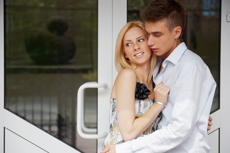 舒适的年轻夫妇拥抱在家门口，看着外面
