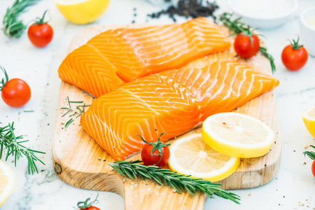 木制砧板上的生鲜鲑鱼肉柳配柠檬西红柿和其他成分健康食品风格