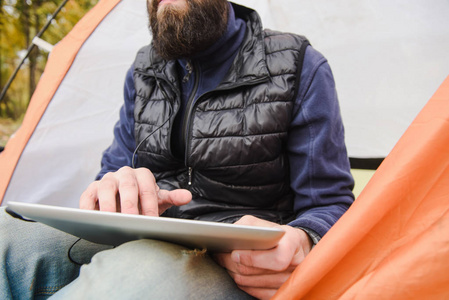 在露营帐篷里使用数字平板电脑的大胡子男子