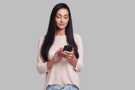 黑发妇女使用智能手机站立反对灰色背景