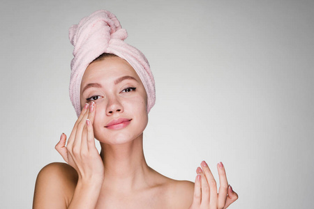 有吸引力的年轻女孩用粉红色的毛巾在她的头上应用保湿面