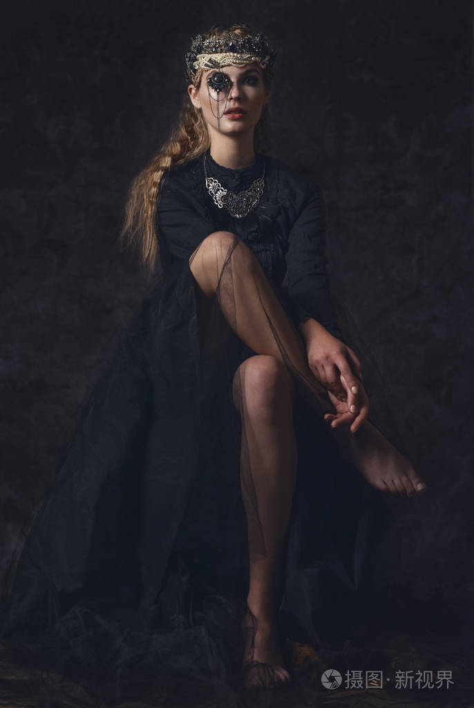 在黑暗的哥特式背景上的黑色幻想服装的黑暗女王高时尚美女模特与黑暗