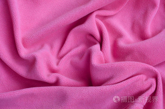 毛茸茸的粉色羊毛布的毯子.浅粉色软毛绒绒材料的背景与许多浮雕褶皱