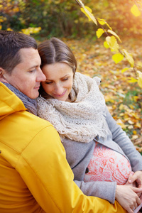 怀孕的女人和男人放松在秋天的公园