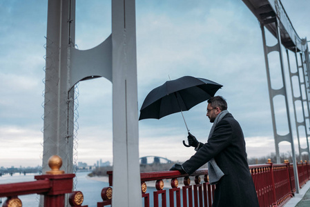 站立在桥梁的英俊的孤独的人与伞