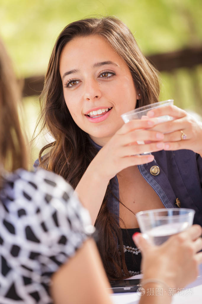 有表现力的年轻的成年女子喝酒, 并与她的朋友在户外交谈