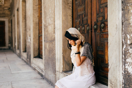 一个戴围巾的年轻女子坐在清真寺的门槛上