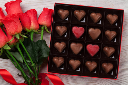 情人节贺卡与红玫瑰和心巧克力盒在木桌上。顶部视图