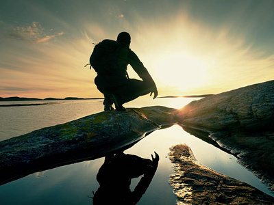 孤独的徒步旅行者独自一人坐在海边享受日落。查看岩石悬崖到海洋