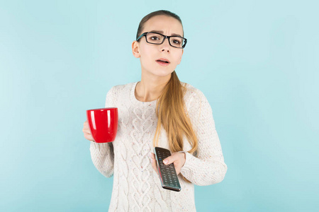 漂亮的女孩在时尚的眼镜捧着杯茶和遥控器