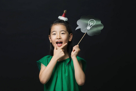 可爱的亚洲女孩穿着绿色的礼服, 手持一个想法灯泡棍子与圣诞节头装饰黑色背景。我认为一个好主意