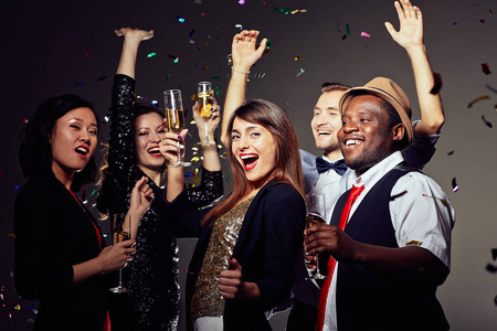 多民族的朋友一起无比的香槟长笛, 祝新年快乐, 在夜总会玩得开心, 五彩纸屑飘落