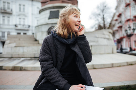 欢快的金发女郎的肖像在她的手机上说话, 一边快乐地看着城市街道孤立