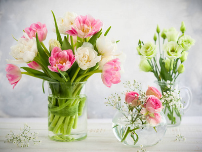 美丽的花朵捧在花瓶上的木桌上。郁金香玫瑰和洋
