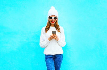 妇女使用智能手机在白色毛衣, 帽子上的蓝色 backgr