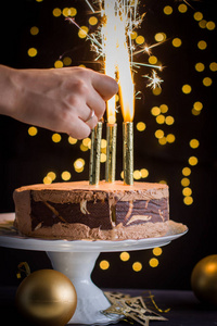 巧克力慕斯蛋糕装饰与燃烧的烟花。圣诞彩灯的背景。大气节日贺卡