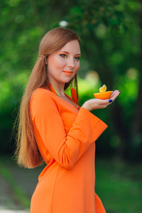 美丽的红色头发的妇女与多汁的美味橙在夏季绿色公园的肖像