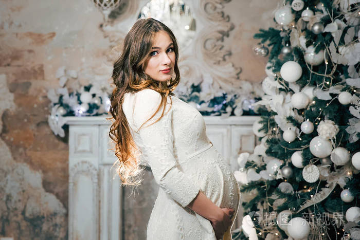 怀孕的妇女抱着一个腹部附近的圣诞树与灯