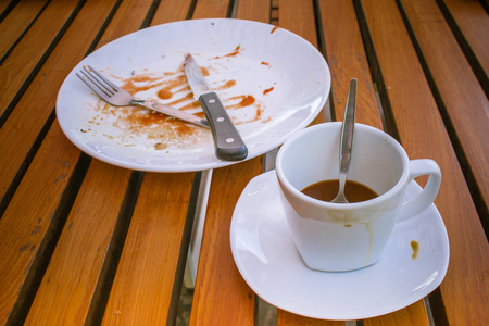 关闭肮脏的咖啡杯和勺子设置在白色的碟子, 刀和叉子, 在白色的脏盘子。他们在木桌吃早餐在早晨在复古样式