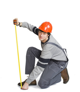 一个年轻男子在工作的灰色衣服和橙色安全帽测量房间的公制面积