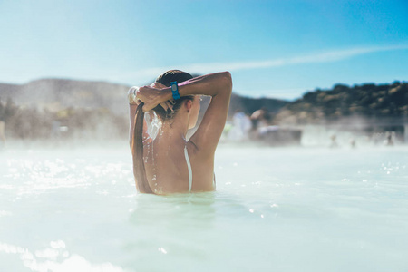 在冰岛的热水池里放松的少妇的后方看法