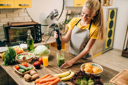 在厨房做饭的妇女, 混合健康的有机食品在玻璃。素食, 新鲜蔬菜和水果在木桌上