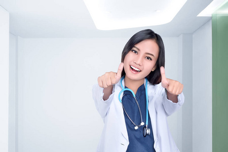 美丽的亚洲女医生在白色外套显示大拇指在诊所室