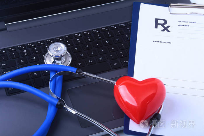 一个医疗听诊器附近的笔记本电脑与红色的心在一个木桌上, 白色