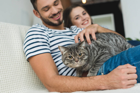 快乐的年轻夫妇与可爱的花猫坐在沙发上