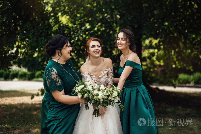 新娘和伴娘穿着礼服站在婚礼当天的绿色公园