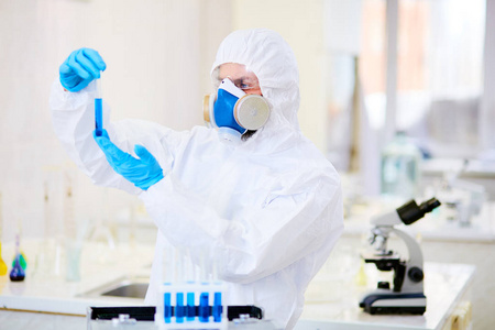 自信的化学家穿着套装和呼吸器研究有毒液体的试管, 现代实验室的内部背景