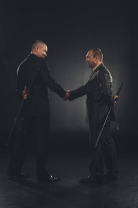 背后刀侧视图的黑社会成员握手与刀背后孤立黑色照片