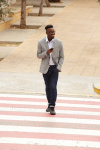 超酷年轻黑人商人在城市里用手机行走的全长画像