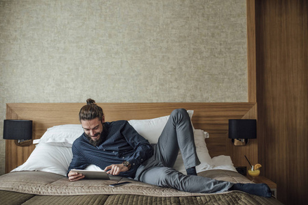 英俊的白种商人自由职业者躺在酒店床上使用平板电脑