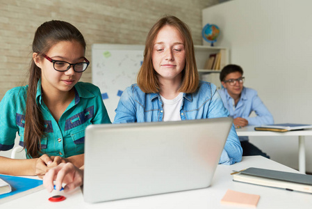 聪明的十几岁的学生穿着休闲服使用笔记本电脑, 而有 Ict 类, 他们的男同学在眼镜坐在他们身后, 看着相机